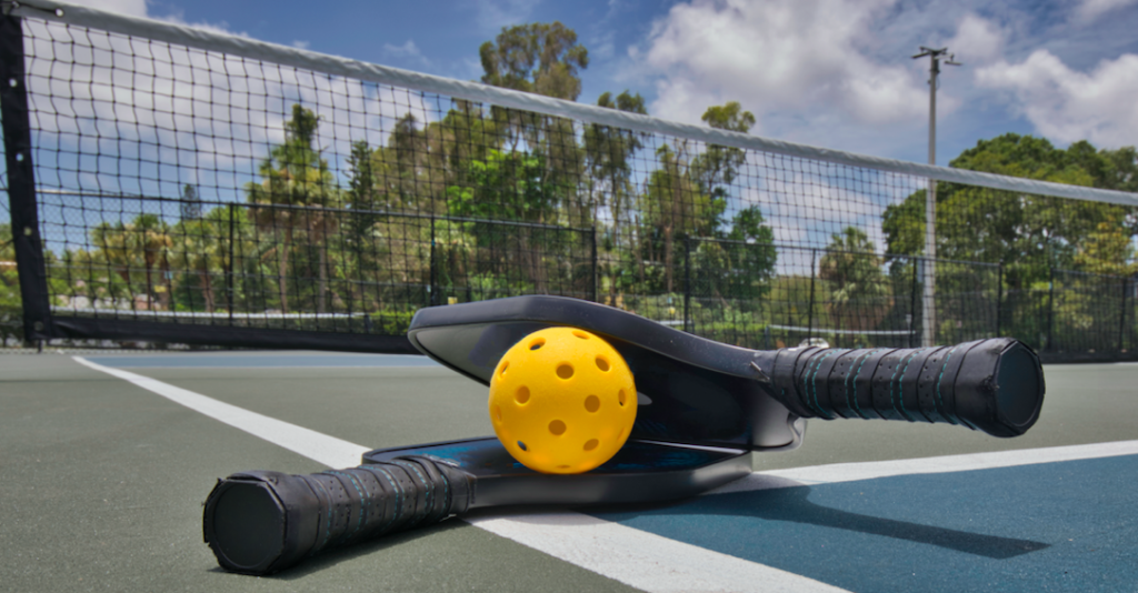 The history of pickleball. Two paddles laying on a court in this image.