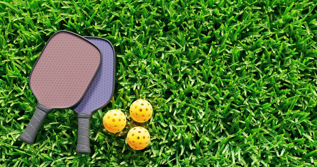 Can I play pickleball on grass? Two pickleball paddles on grass.